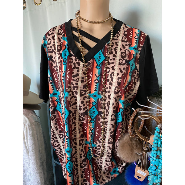 aztec print on a top with black sleeves. print is brown, turquoise and orange. two slanting strips on neckline. 